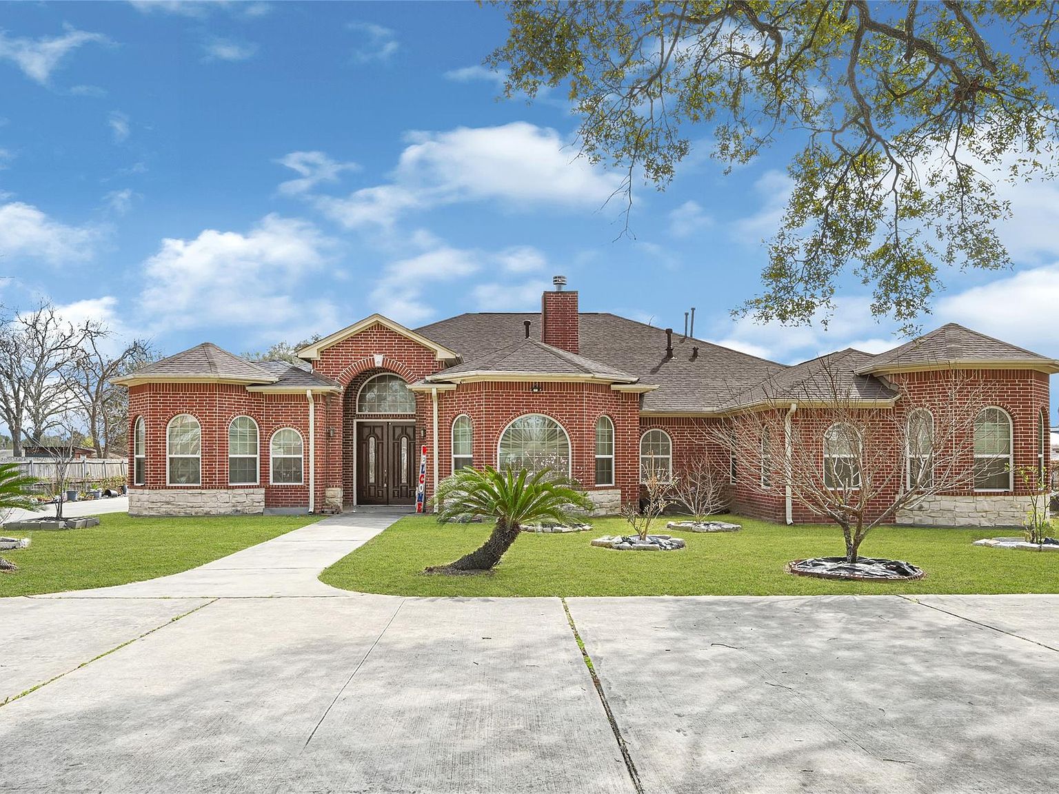 Front elevation of 6519 Breen Dr, a full-brick single-story estate with arched windows, a chimney, and a palm-tree-framed driveway in Northwest Houston